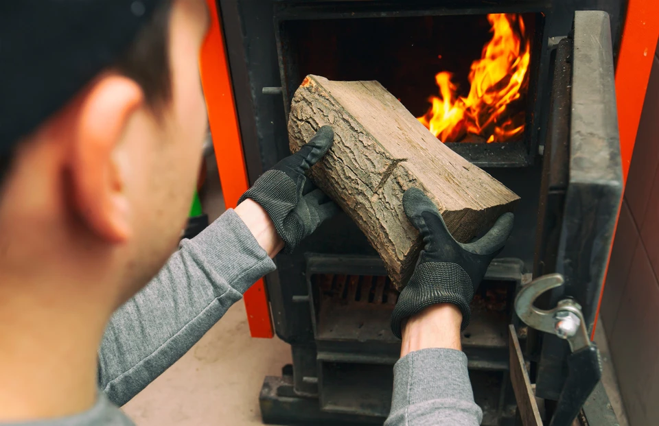 Une personne charge du bois de chauffage dans un poêle à bois domestique, portant des gants de protection thermique