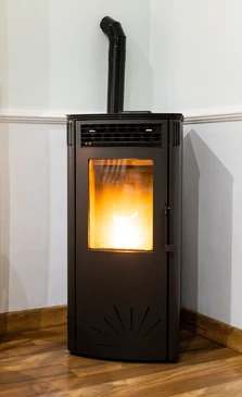 Intérieur résidentiel avec poêle à granulés noir en fonctionnement, flammes visibles à travers la vitre, installé dans angle de pièce sur parquet bois