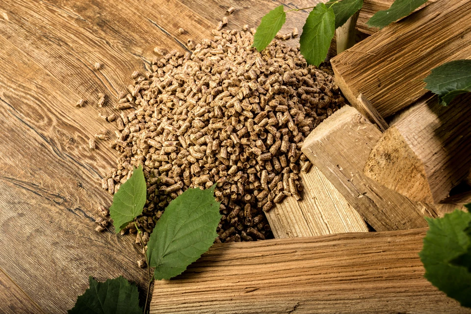 Scène intérieure montrant des granulés de bois disposés dans un panier en osier tressé avec anses en corde naturelle, débordant sur une surface en bois